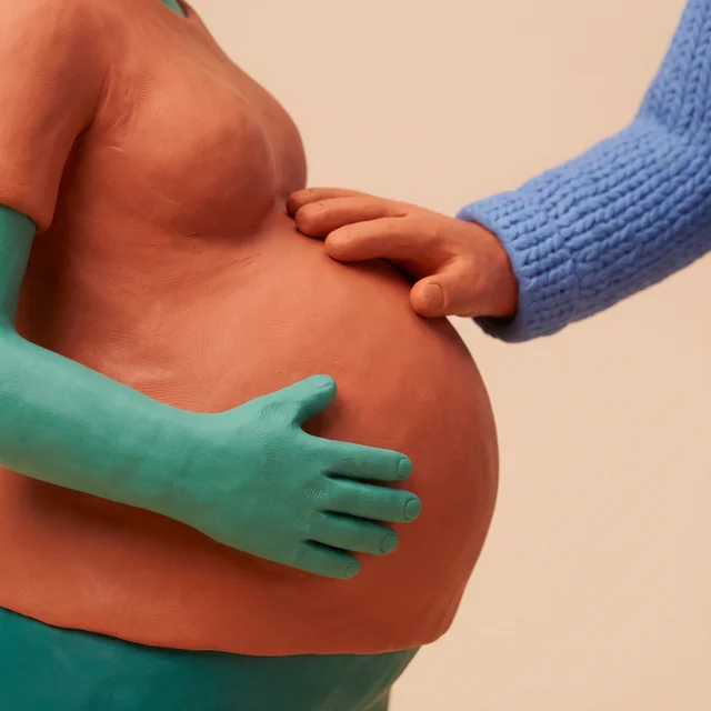 Two clay hands resting on a pregnant belly.